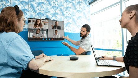 Team in a modern meeting room using video conferencing technology for a hybrid meeting, with in-room participants collaborating with remote colleagues on screen. Ideal setup for huddle rooms and small conference spaces.
