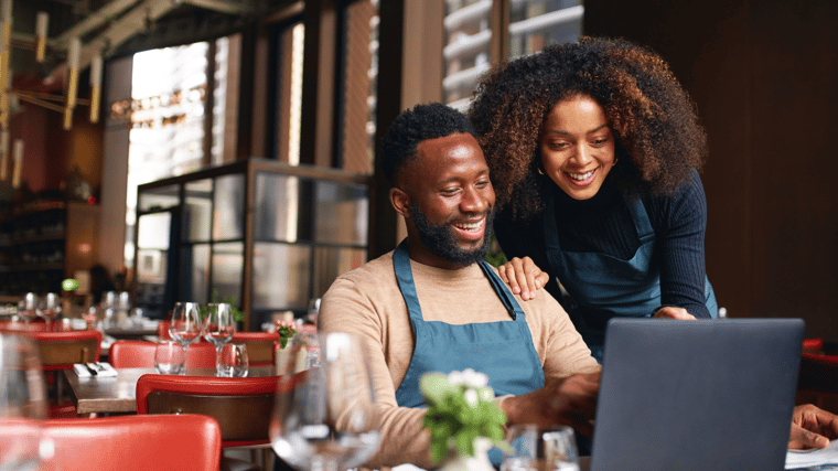 Image of a couple looking at their laptop in a cozy restaurant setting, enjoying a casual meeting or conversation.