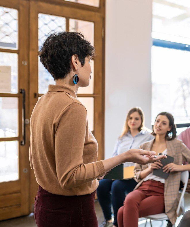 An image featuring a woman lecturer giving a presentation to a group of businesspeople, showcasing engaging collaboration. 