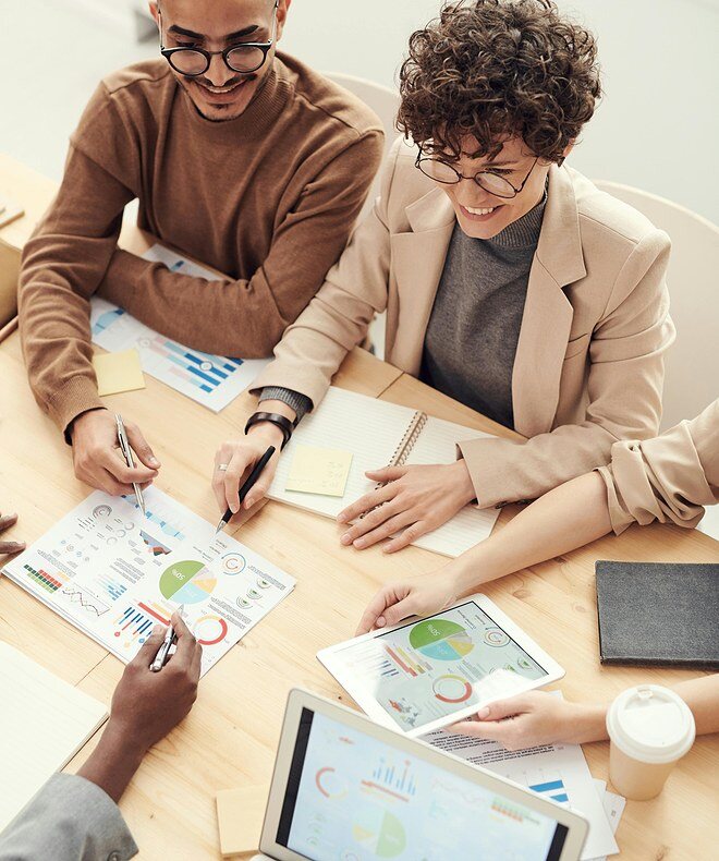 A group of coworkers gathered around a conference table, attentively discussing information regarding a project. Utilizing Boom Collaboration Equipment, they enhance communication and productivity during the meeting