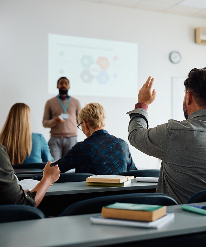 Image showcasing a student raising his hand to answer the teacher's question during an education training session, demonstrating active engagement. 