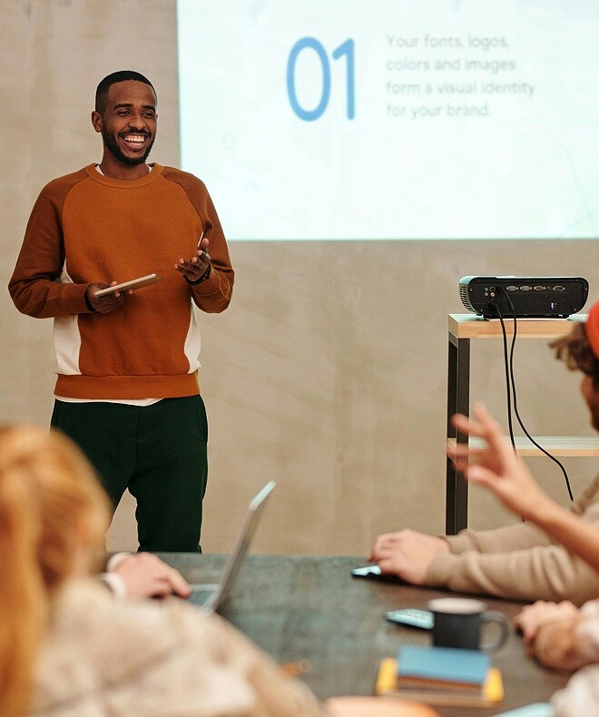 Happy employee presenting his project to coworkers using Boom-enabled video conferencing kit in a huddle room.
