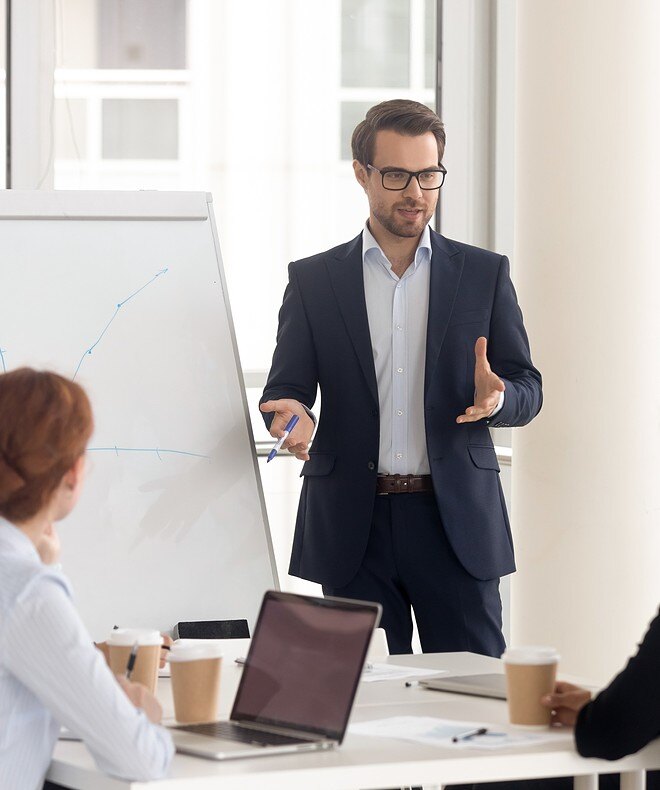 A male business coach in a suit giving a presentation with a flipchart, enhanced by Boom equipment for clear audio and seamless communication.