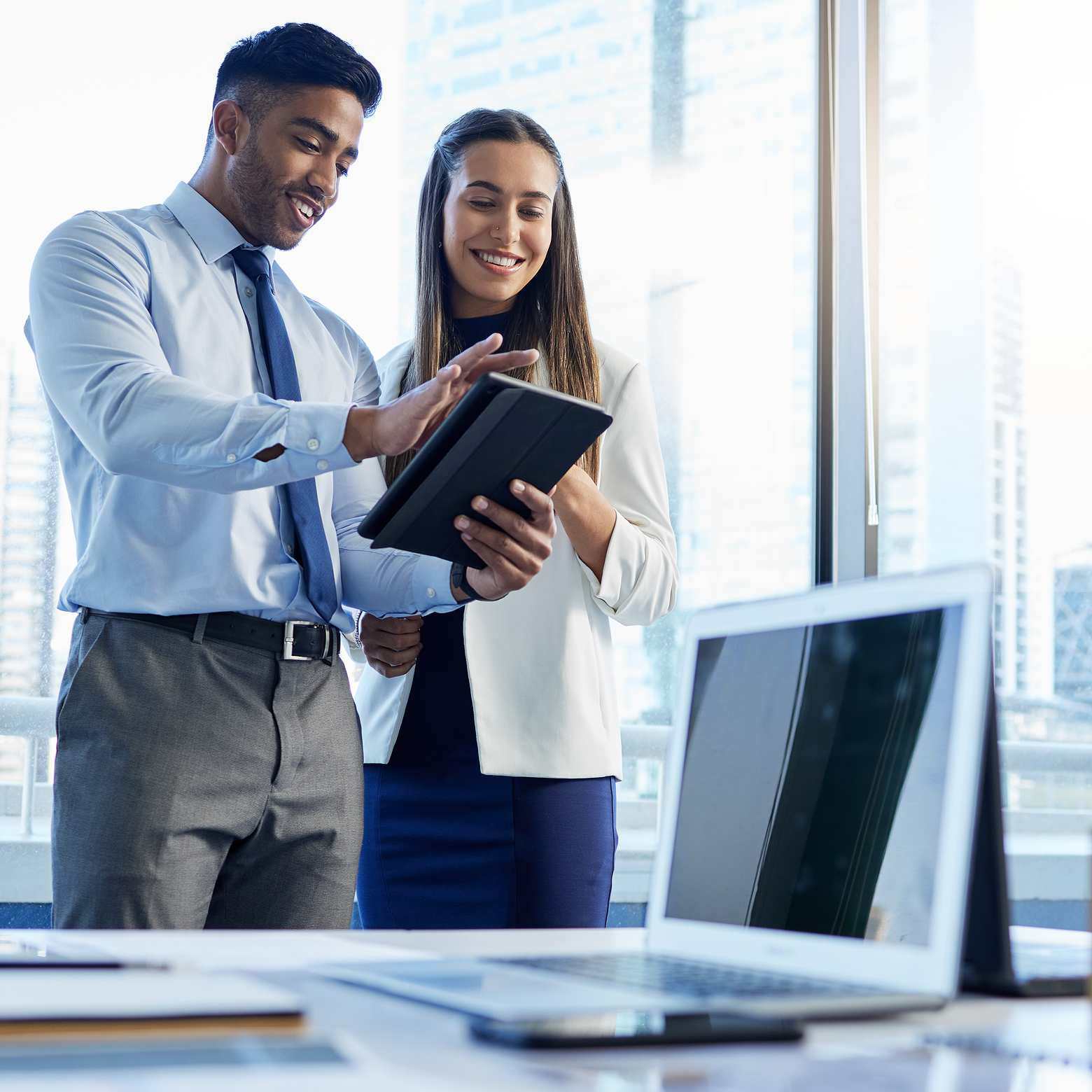 Image of two business people discussing a project on a digital tablet, highlighting collaboration and modern technology. Boom Collaboration Equipment enhances meetings’ quality by providing reliable and high-quality technology.