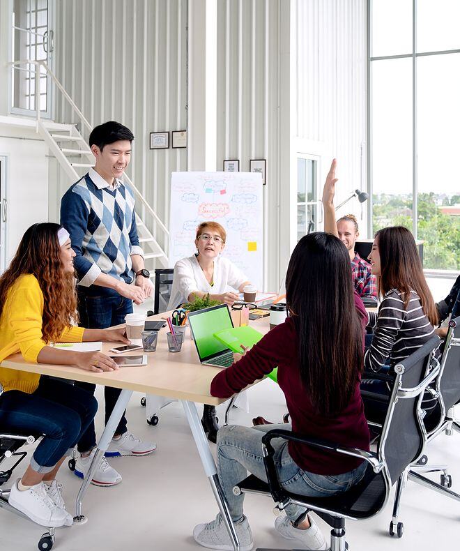 A group of young creative team members engaged in discussion, smiling, and laughing during a brainstorming session. 